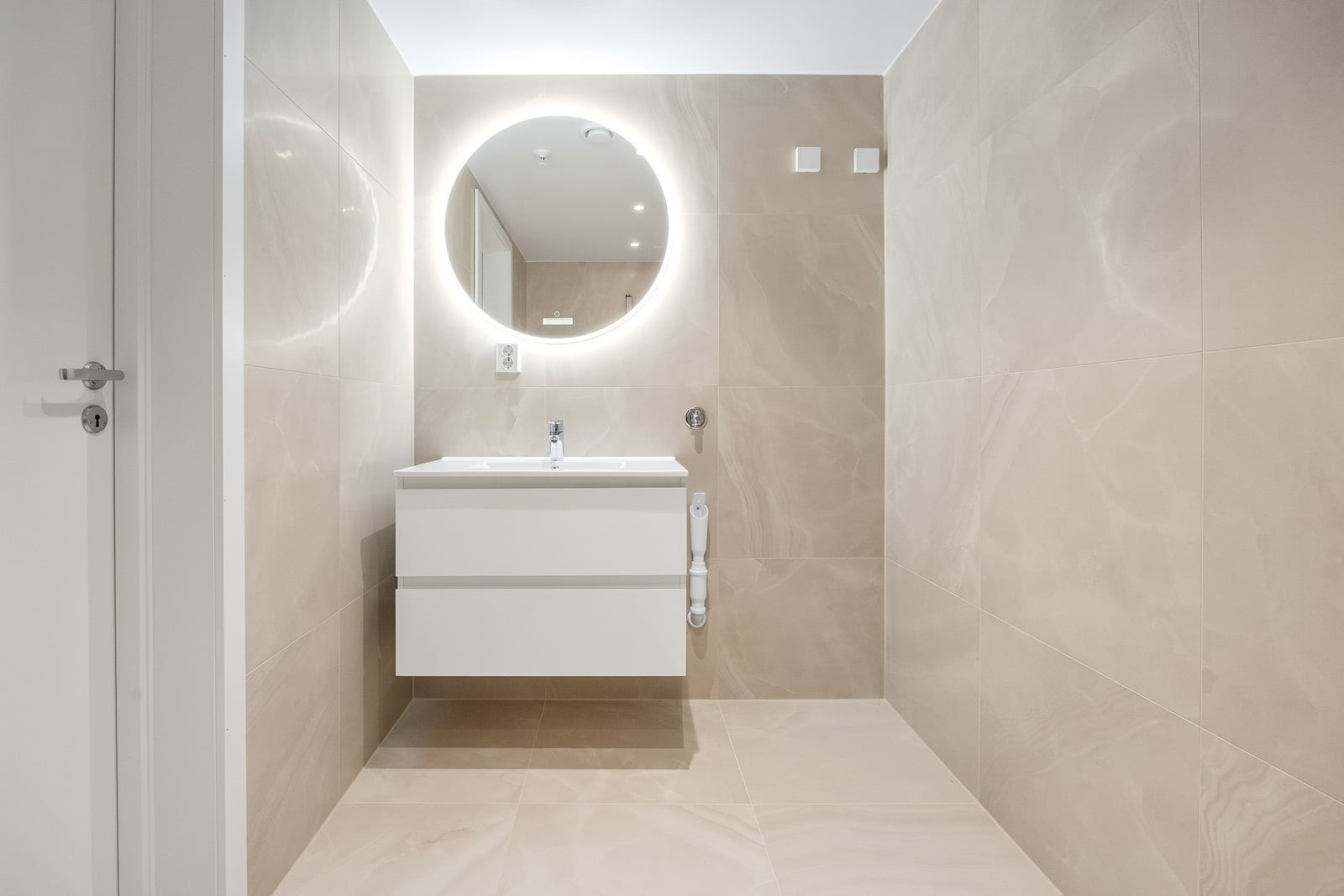 Delikat, flislagt bad med servant og speil med integrert belysning. Galleribilde