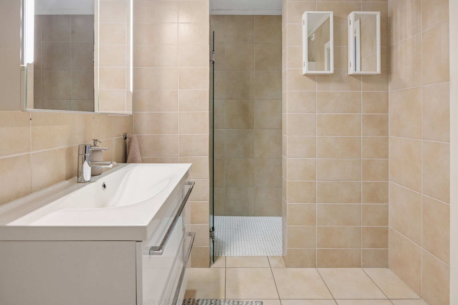 Badet er utstyrt med vegghengt toalett, servant med speilskap over og en romslig dusjsone. Galleribilde