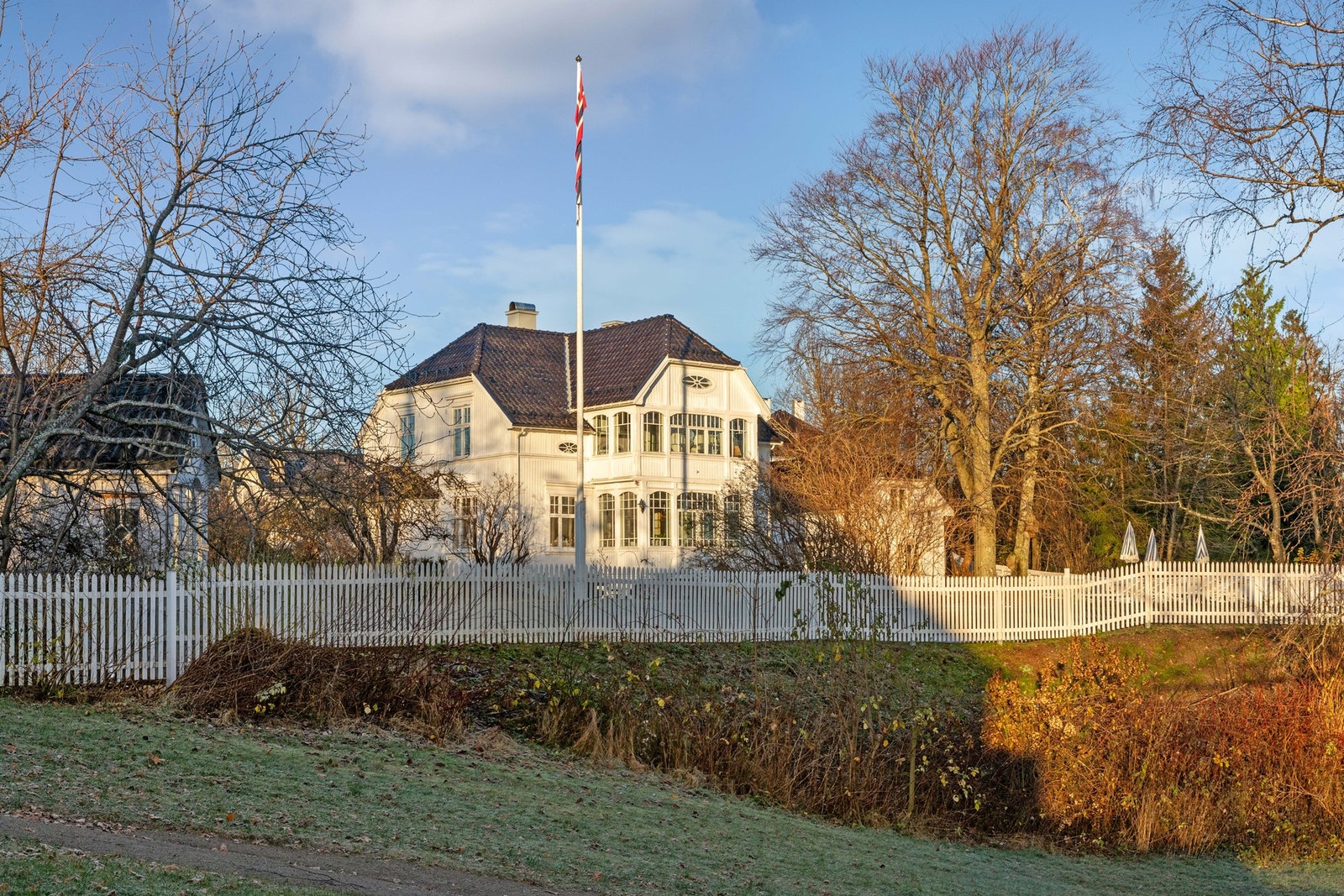 Tomten er på over 3,3 mål og fremstår som en parkmessig eiendom, vakkert rammet inn av et hvitmalt stakittgjerde fra 2024. Galleribilde