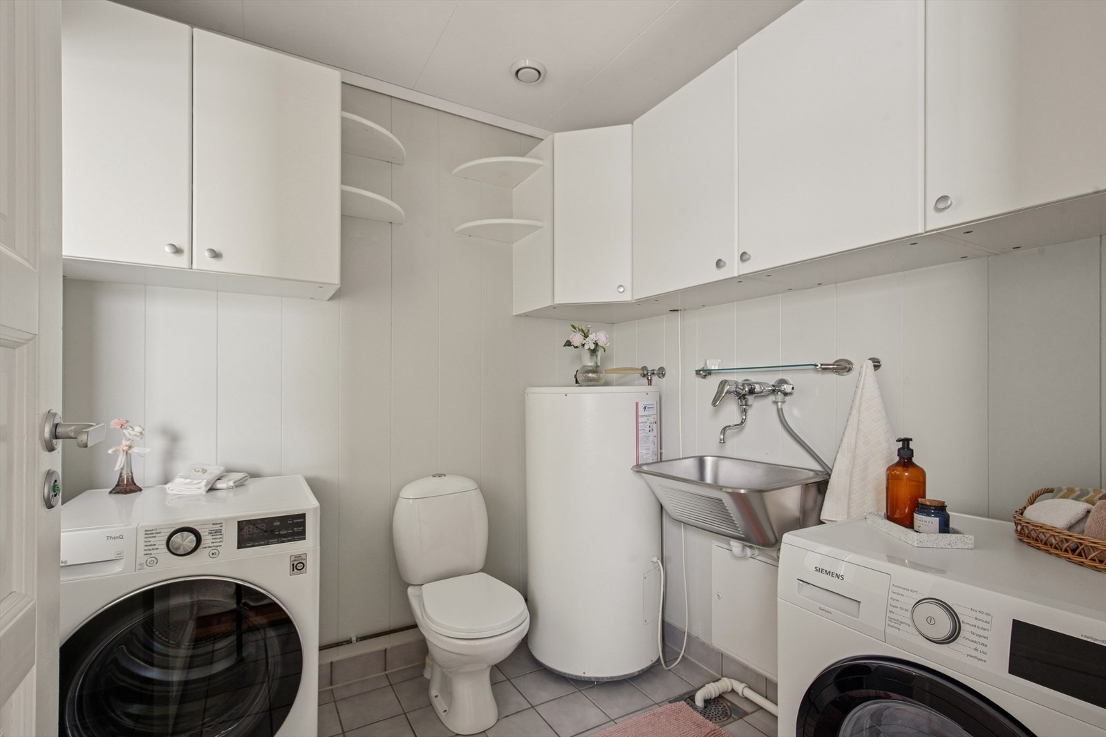 Praktisk vaskerom med flislagt gulv og gulvvarme, opplegg for vaskemaskin og god skapplass. Galleribilde