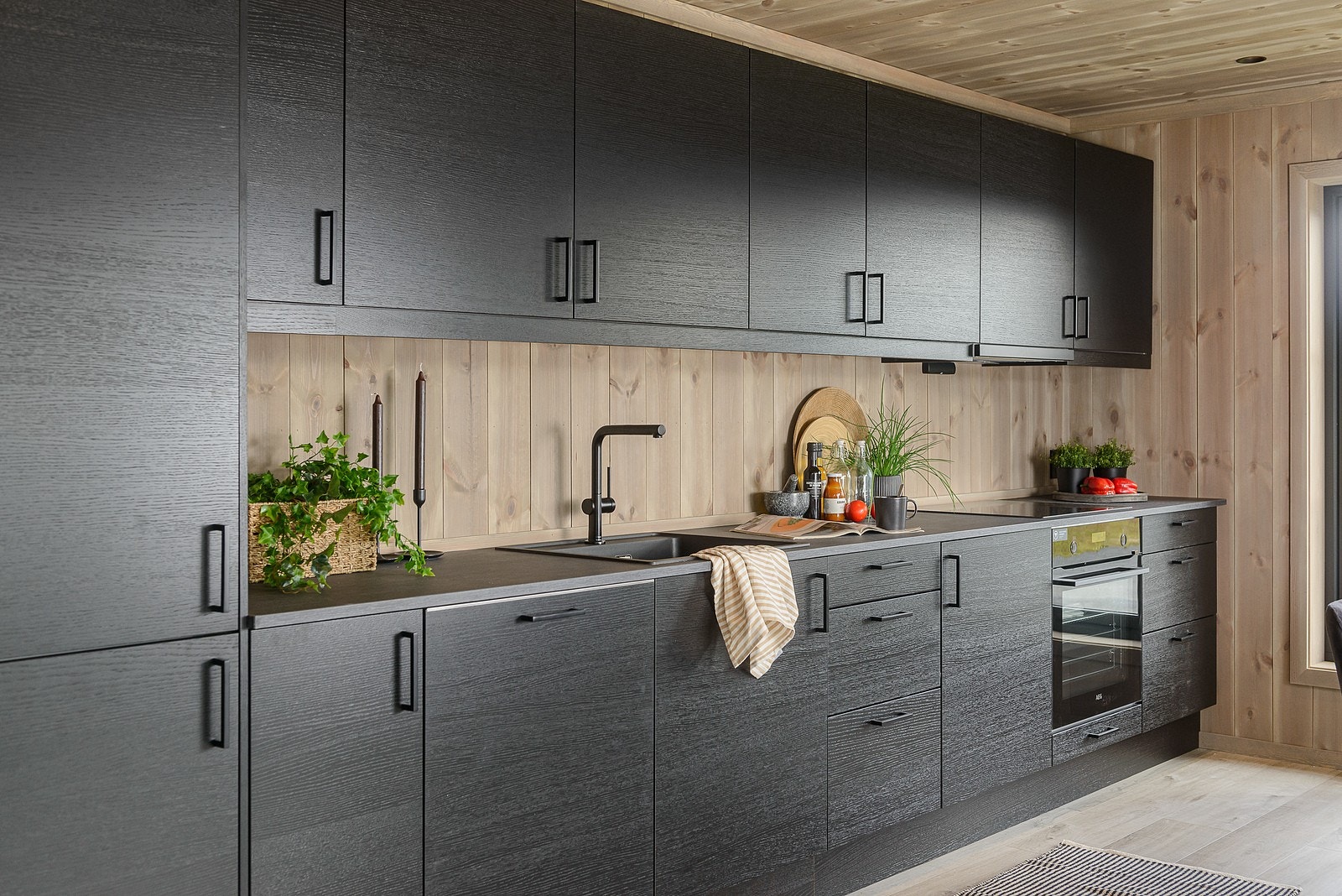 Mørk, stilig kjøkkeninnredning med glatte fronter og mørk, laminert benkeplate med nedfelt kjøkkenkum og platetopp. Galleribilde