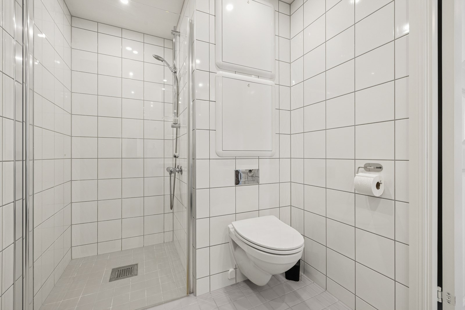 Badet er utstyrt med veggmontert toalett og et dusjhjørne med innfellbare glassdører. Galleribilde