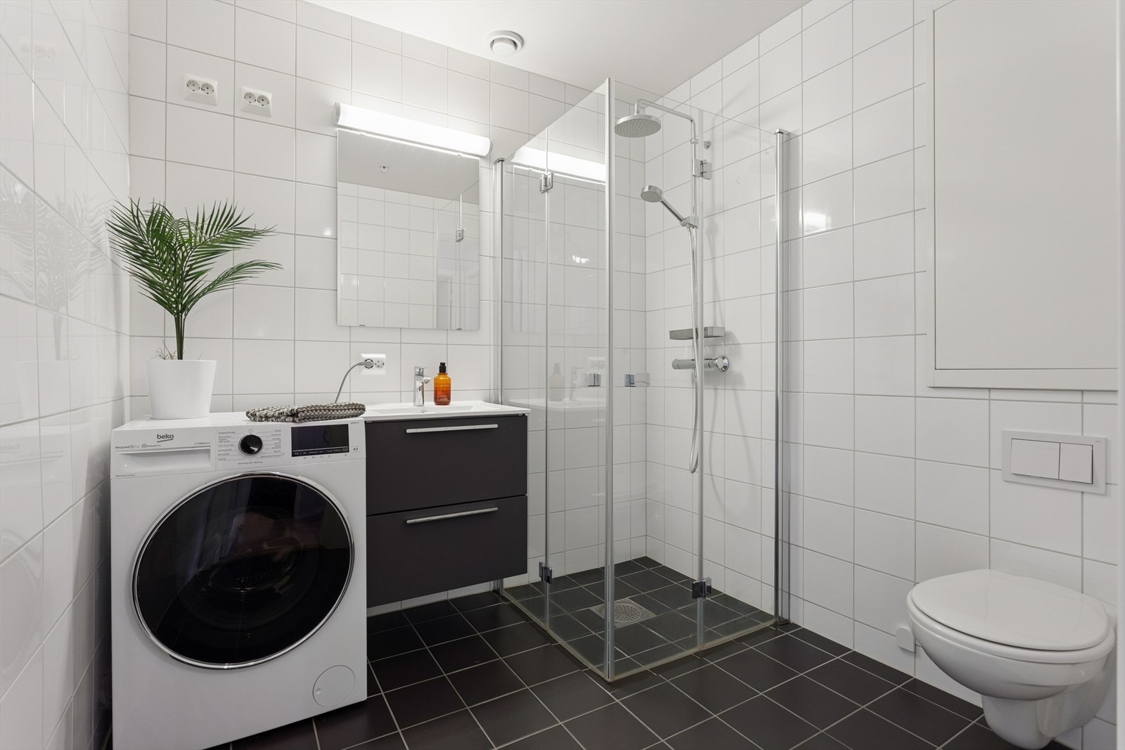 Badet er stilrent med tidløs baderomsinnredning, vegghengt toalett og dusjhjørne. Her er det naturligvis opplegg for både vaskemaskin og tørketrommel og gulvvarme. Galleribilde