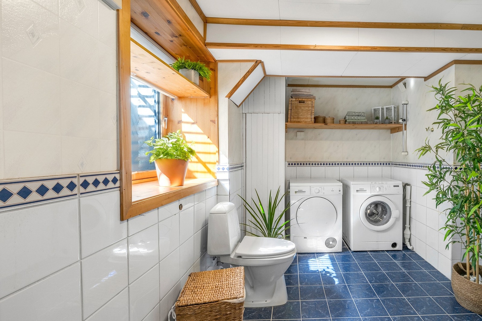 Flislagt bad/vaskerom. Her er det opplegg for både vaskemaskin og tørketrommel, god benkeplass og praktisk hyllesystem for oppbevaring. Galleribilde