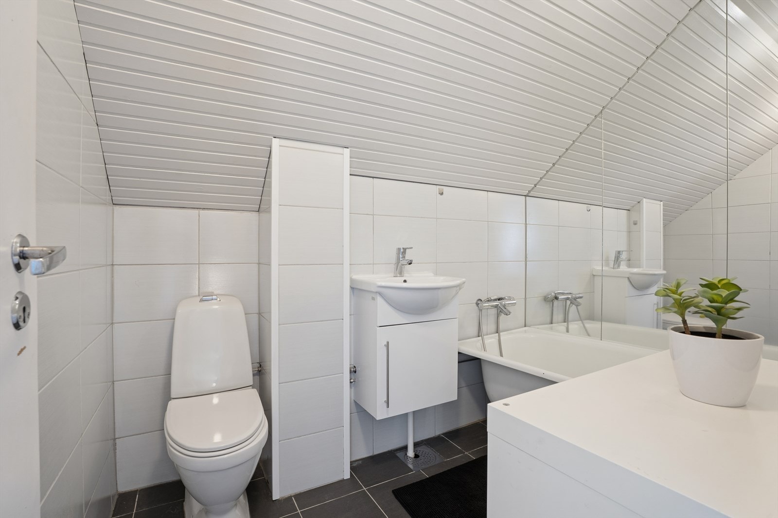 Våtrom i 2. etasje. Badet har flislagt gulv med gulvvarme. Fliser på vegger og malt panel på innvendig tak. Rommet har baderomsinnredning med heldekkende servant og underskap med dør, frittstående toalett og badekar. Galleribilde