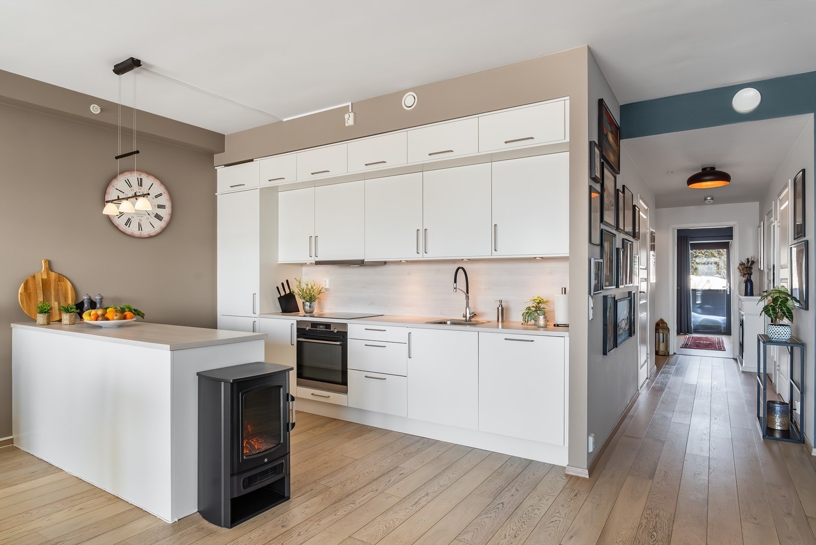 Hvitt, stilrent kjøkken med rikelig skap-, skuffe- og benkeplass. Kjøkkenet er utstyrt med integrerte hvitevarer som stekeovn, platetopp, kombiskap og oppvaskmaskin Galleribilde