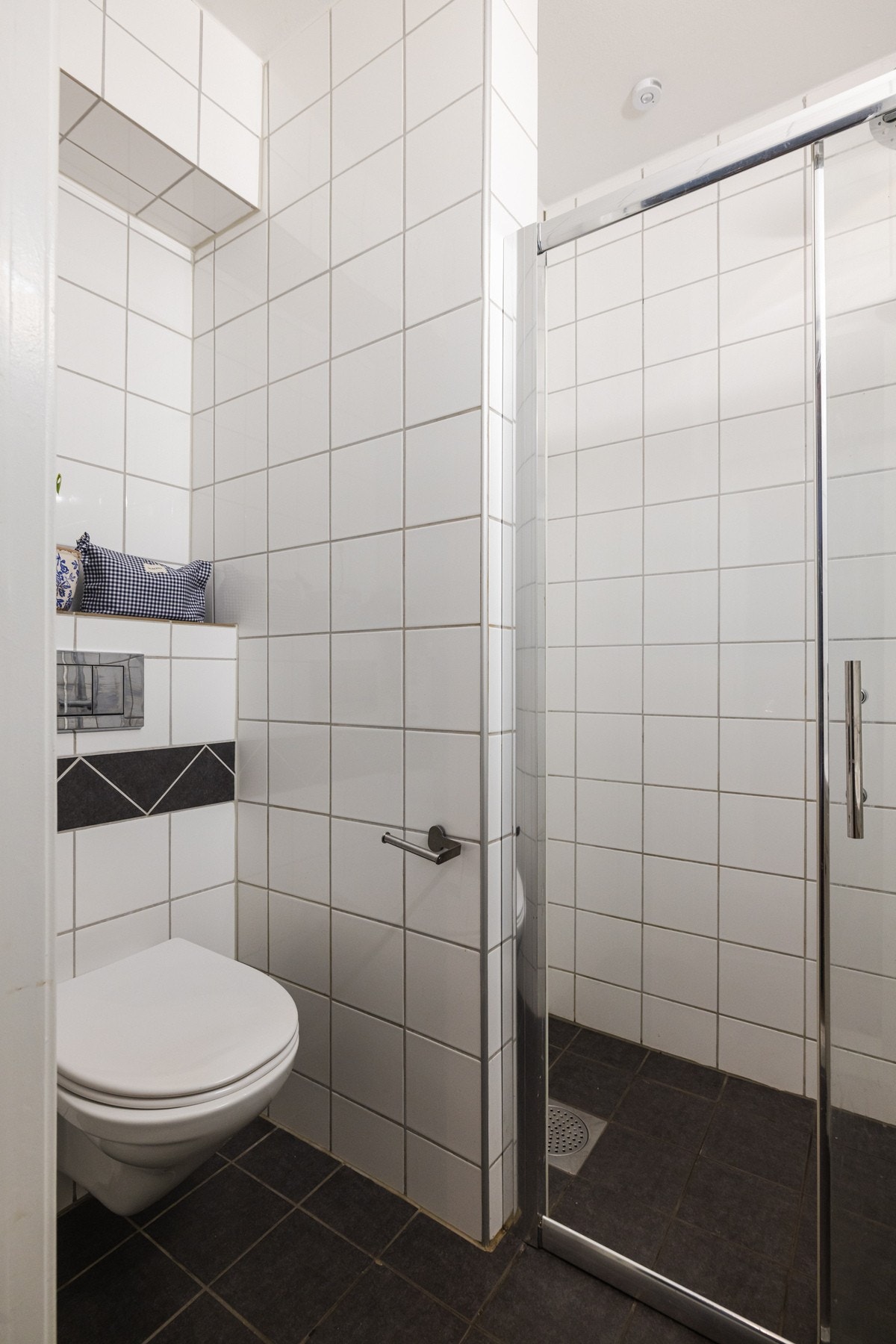 Vegghengt toalett med innebygget sisterne og dusjhjørne med både hånd- og regnfallsdusj som er avgrenset av skyvedør med glassfelt. Galleribilde