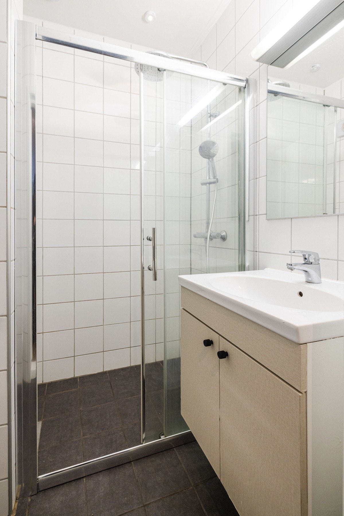 Lyst og pent flislagt baderom har varme i gulvstøp og hvite fliser på vegg. Galleribilde