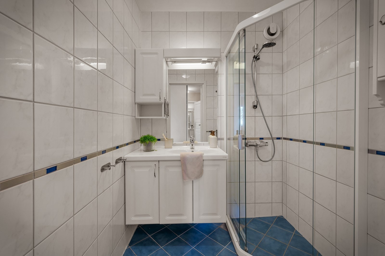 Badet er helfliset med varmekabler i gulv. Her er baderomsinnredning med heldekkende servant og speil med belysning. Badet inneholder også dusjhjørne. Galleribilde