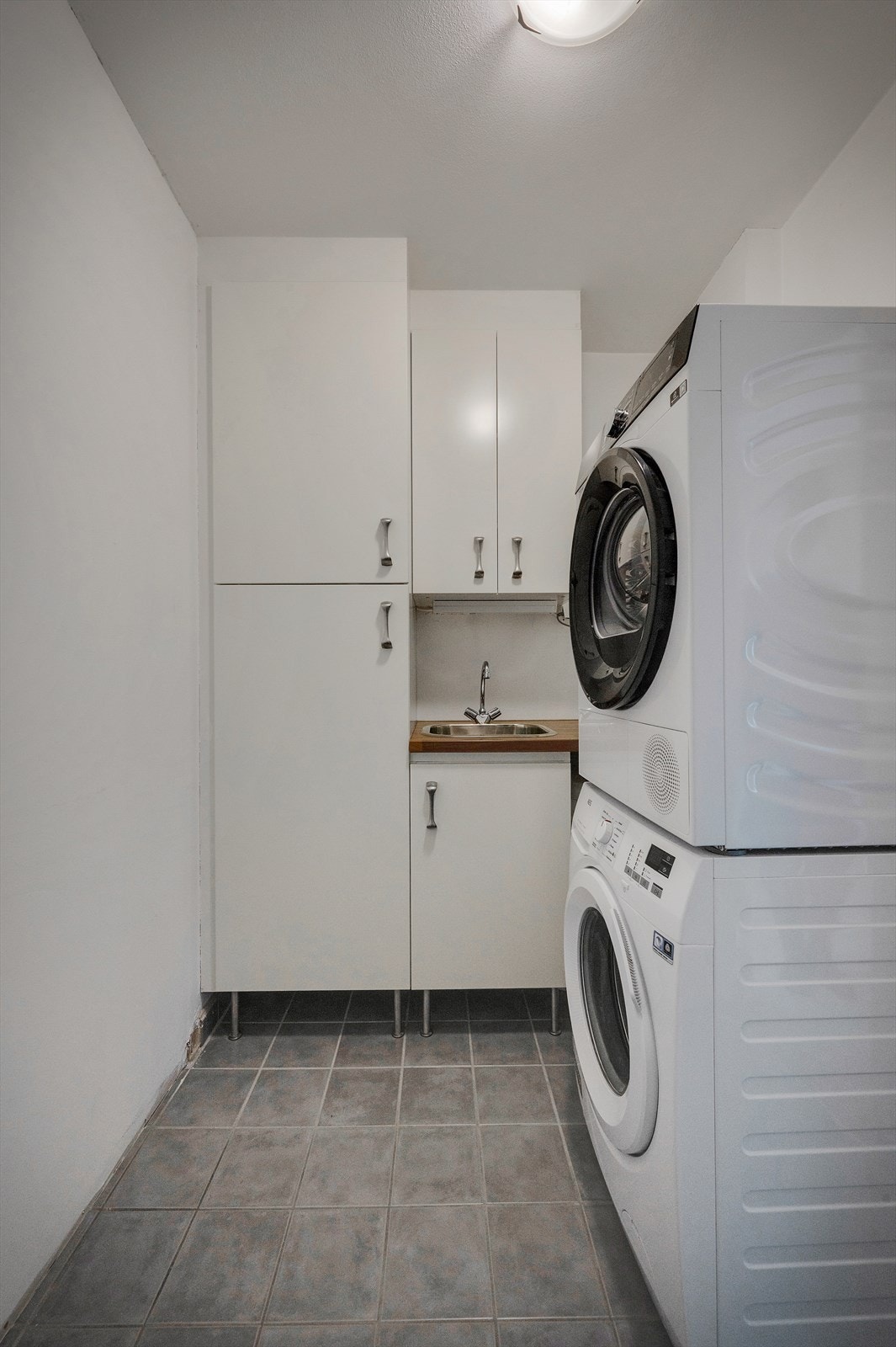 Praktisk separat vaskerom med flislagt gulv og lysmalte vegger. Her er plass til både vaskemaskin og tørketrommel samt god oppbevaring. Galleribilde