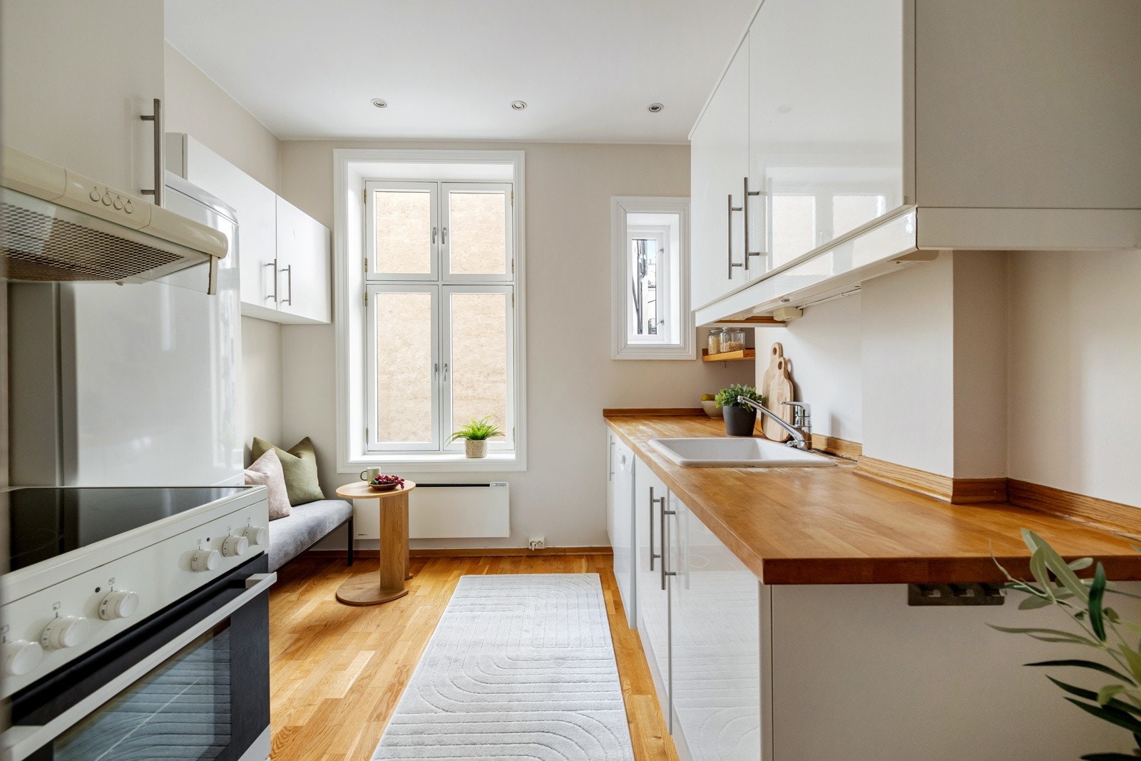 Leilighetens kjøkken ligger i eget rom og er innredet med glatte, hvite fronter og benkeplate av heltre Galleribilde