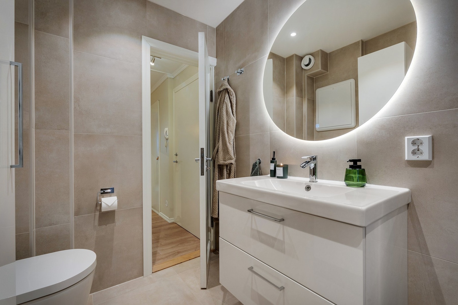 Badet har lekre fliser, baderomsinnredning, veggehengt toalett, inntrekksbare dusjdører og et nydelig belyst speil. Galleribilde