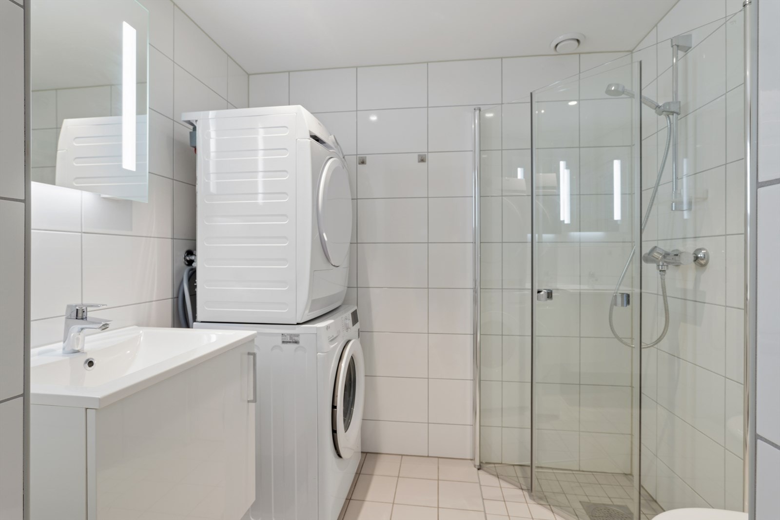 Baderom med flislagte overflater og elektriske varmekabler. Opplegg til vaskemaskin og tørketrommel. Galleribilde