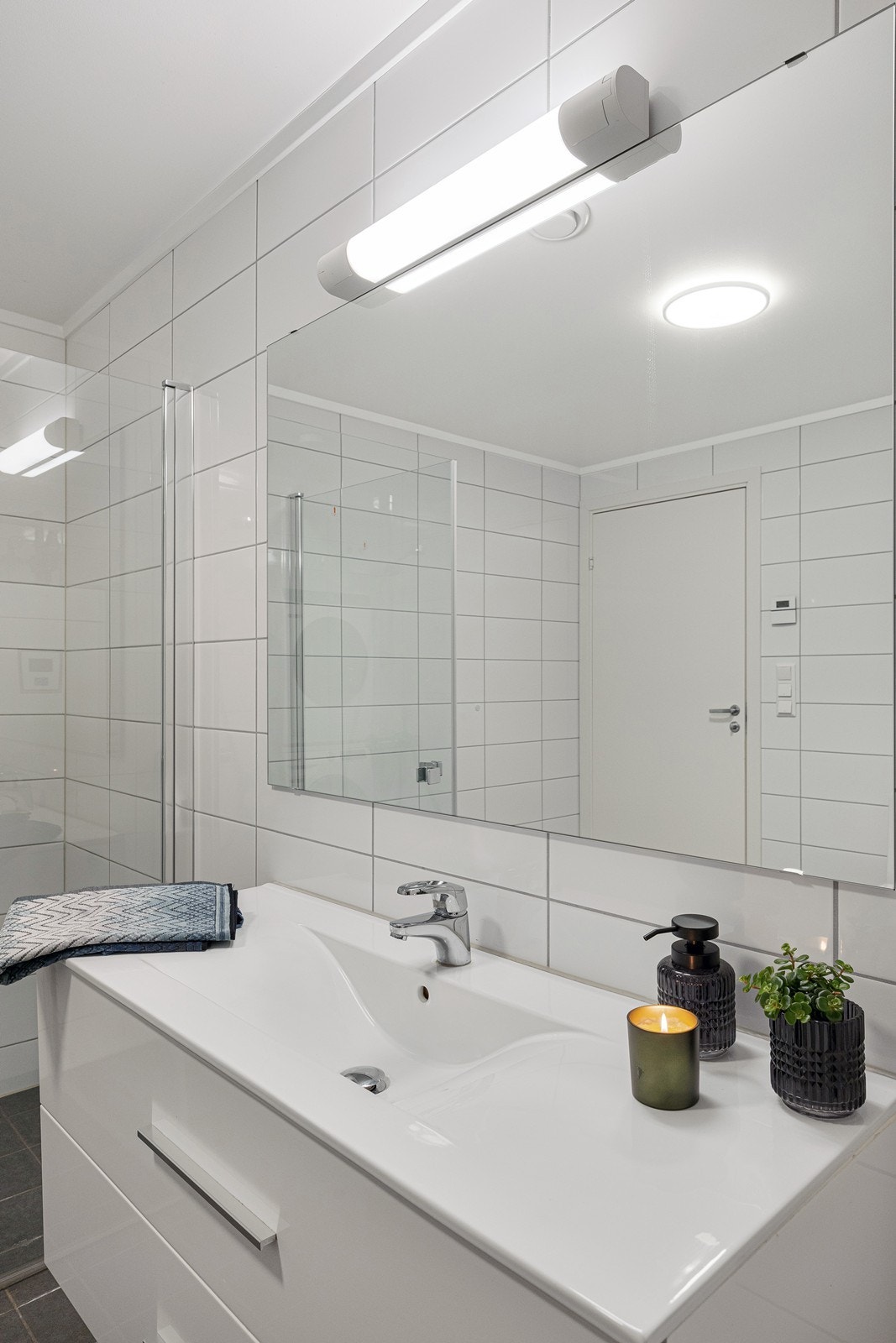 Innredningen har heldekkende servant over hvit skuffeseksjon og speil med belysning. Galleribilde