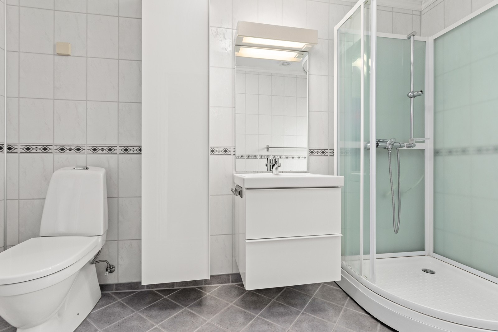 Badet er utstyrt med baderomsinnreiing m/speil, høgskap, dusjkabinett og toalett. Galleribilde