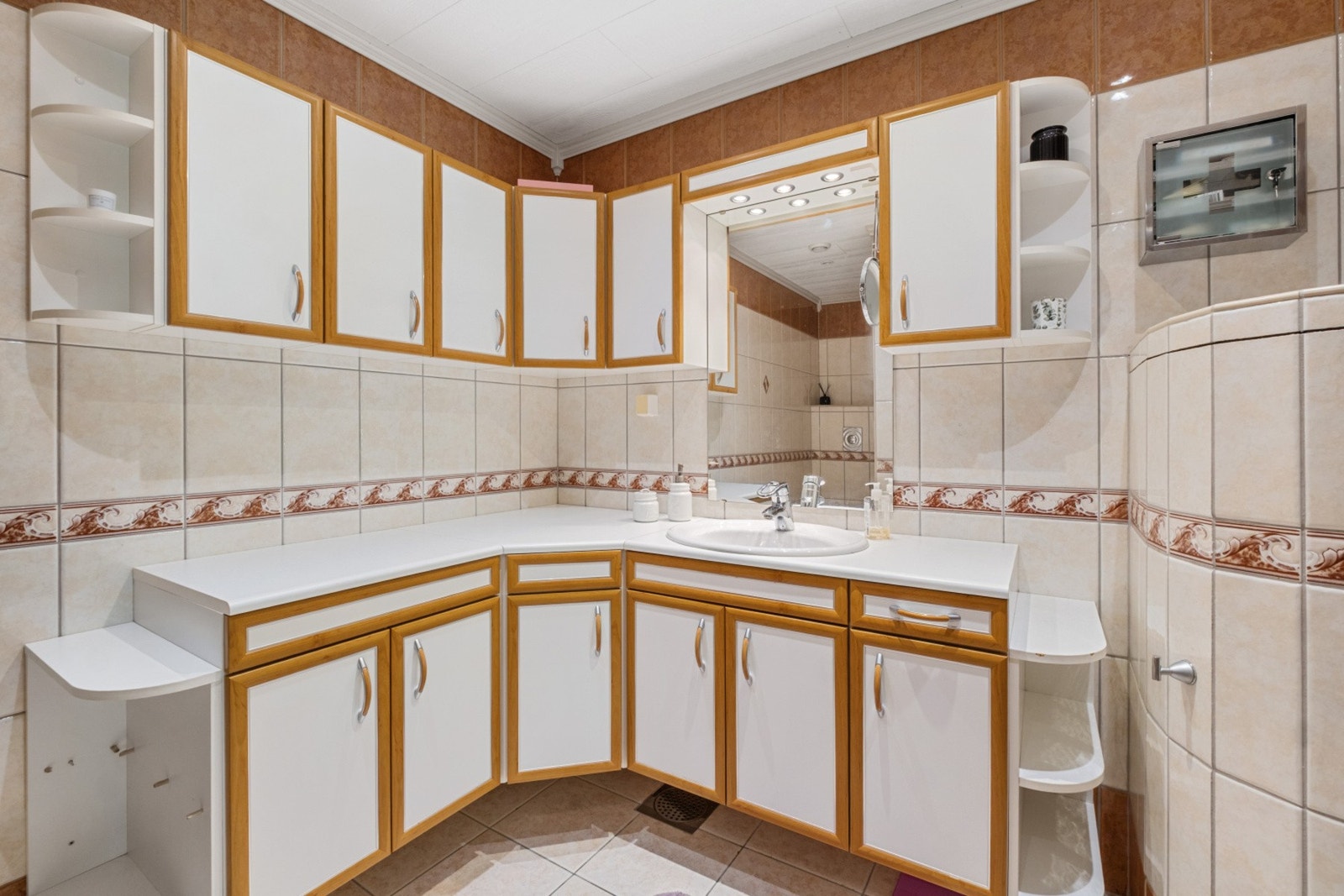 Baderomsinnredning med god skap og benkeplass, ovenpåliggende servant, speil med overlys og stikkontakt over servant. Galleribilde