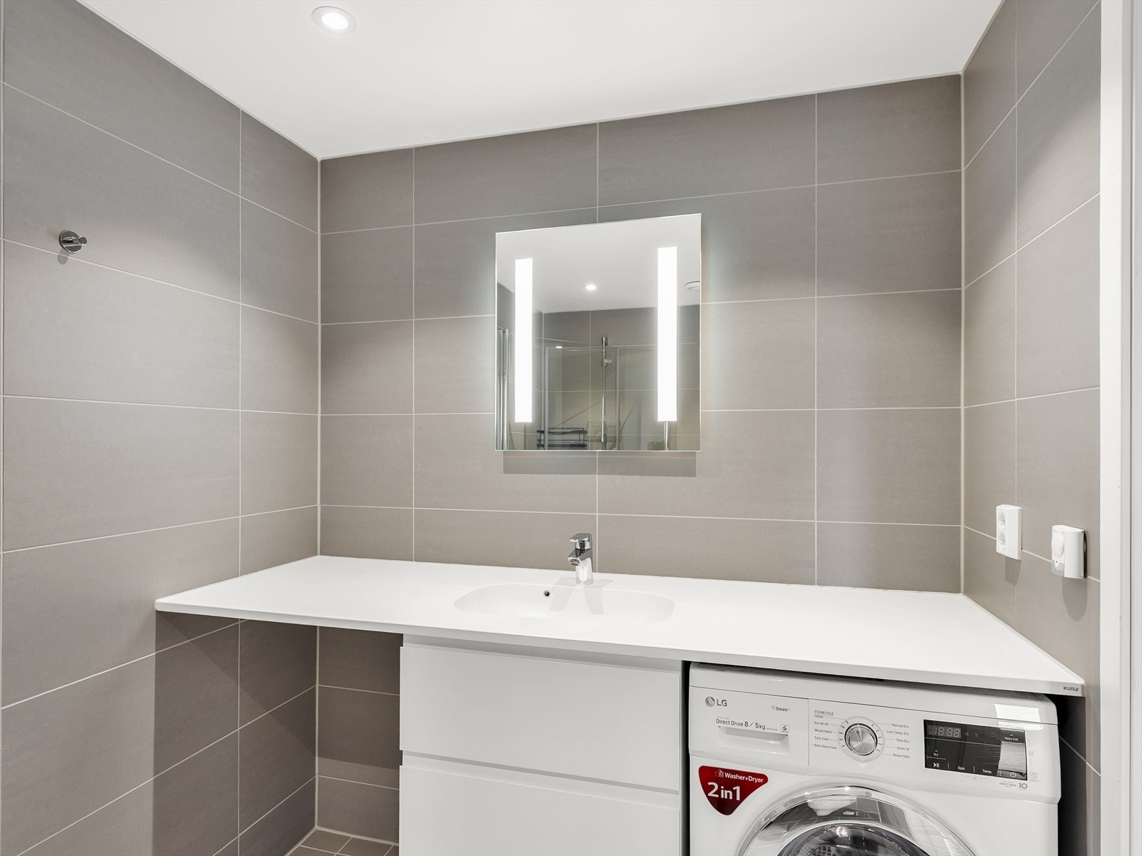 Elegant baderomsinnredning med heldekkende servant, skuffer og praktisk opplegg for vaskemaskin. Galleribilde