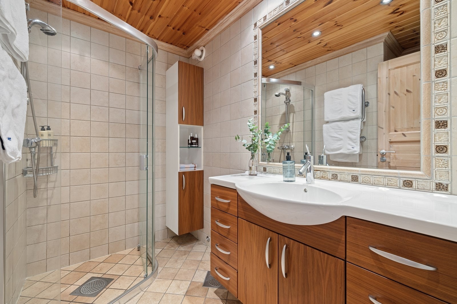 Baderom med dusj, servant med underskap og spotter i taket. Fliser på gulv og vegg. Galleribilde