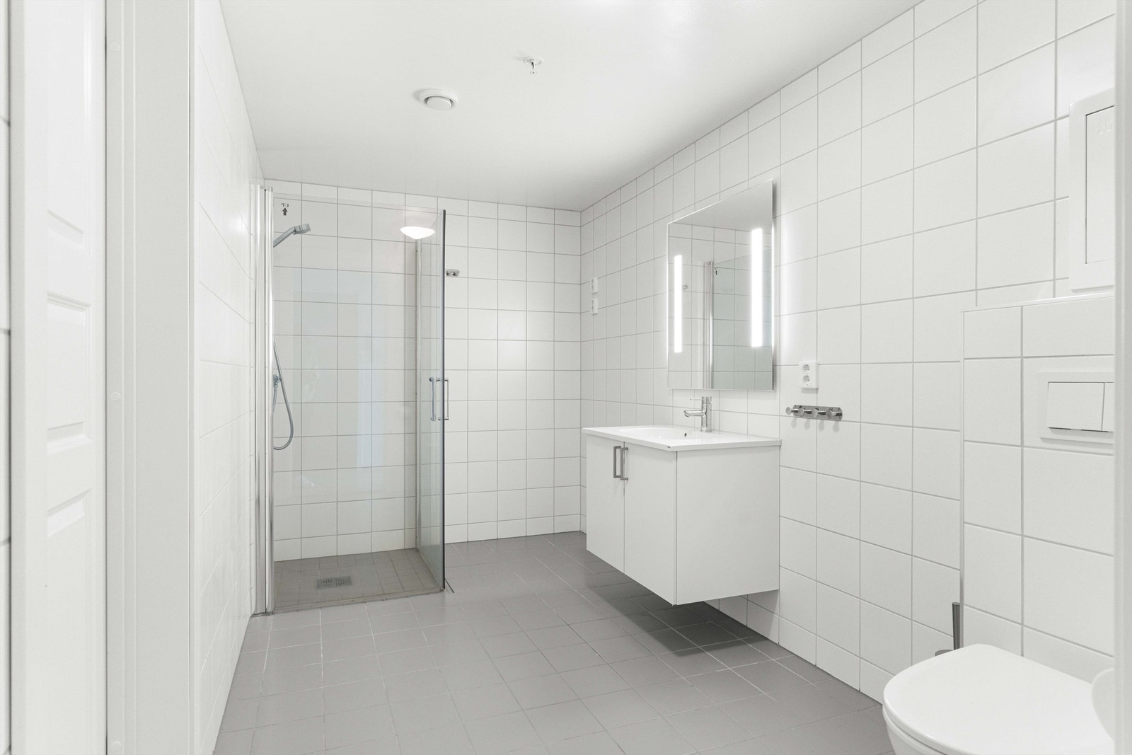 Badet holder en gjennomgående god standard, med fliser på både gulv og vegger samt behagelig gulvvarme. Det er utstyrt med vegghengt toalett og servant med underskap for praktisk oppbevaring. Galleribilde