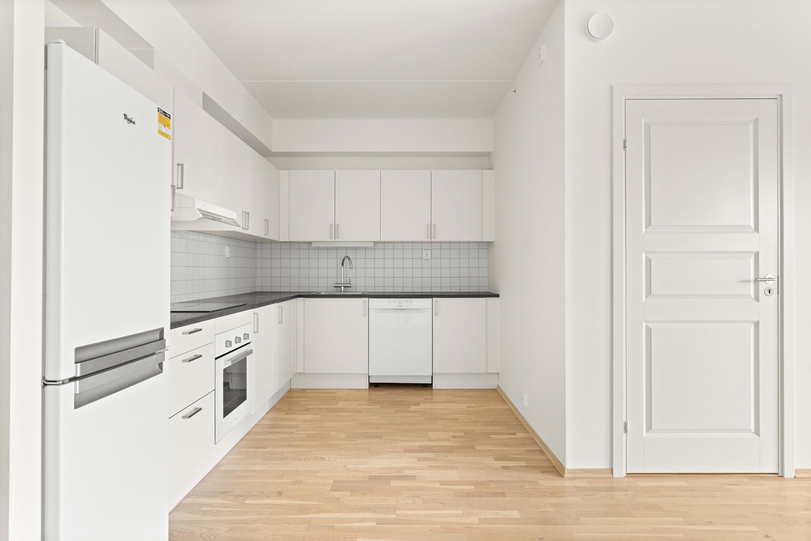 Kjøkkenet er innredet med moderne, glatte fronter og laminert benkeplate. Veggen over benkeplaten er flislagt, og det er belysning over deler av arbeidsflaten. Galleribilde