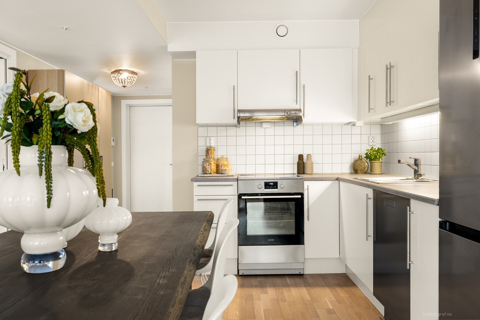 Kjøkkenet er fra Jke Design i hvit slett utførelse. Grå laminat benkeplate med nedsenket vask og fliser mellom benk og overskap. Galleribilde