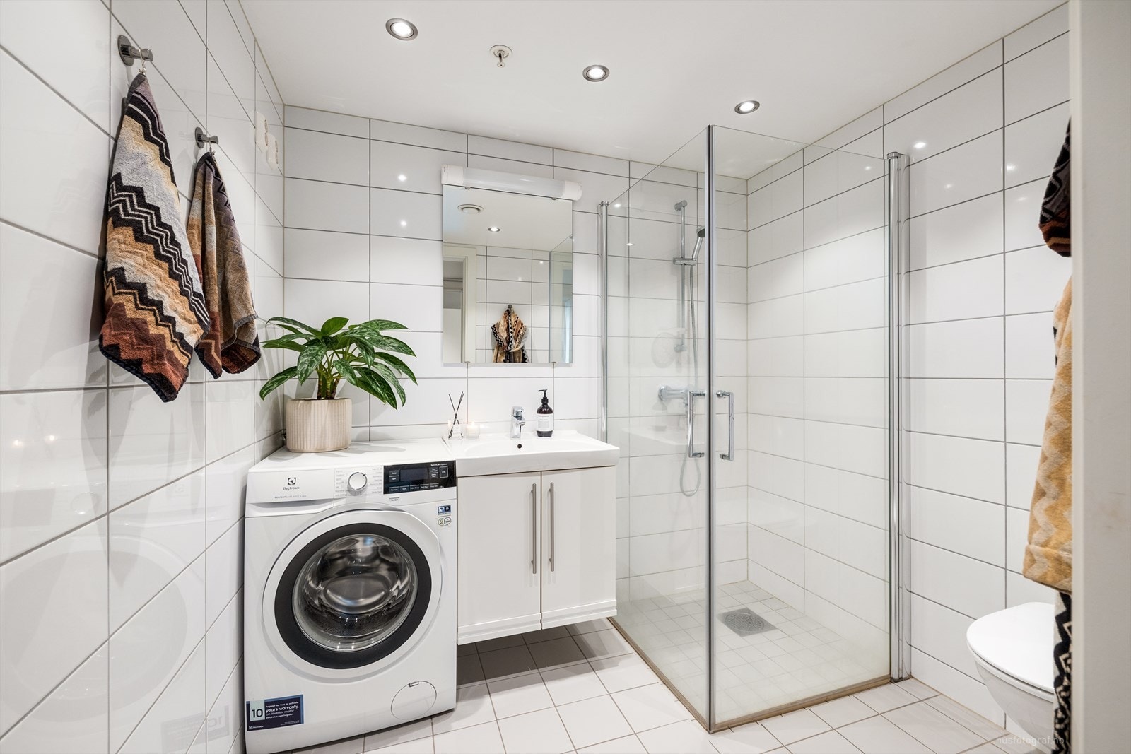 Pent fliselagt bad med varmekabler. Det er montert dusjhjørne med plassbesparende glassdører, vegghengt toalett, servant med underskap og speil med lys. Galleribilde