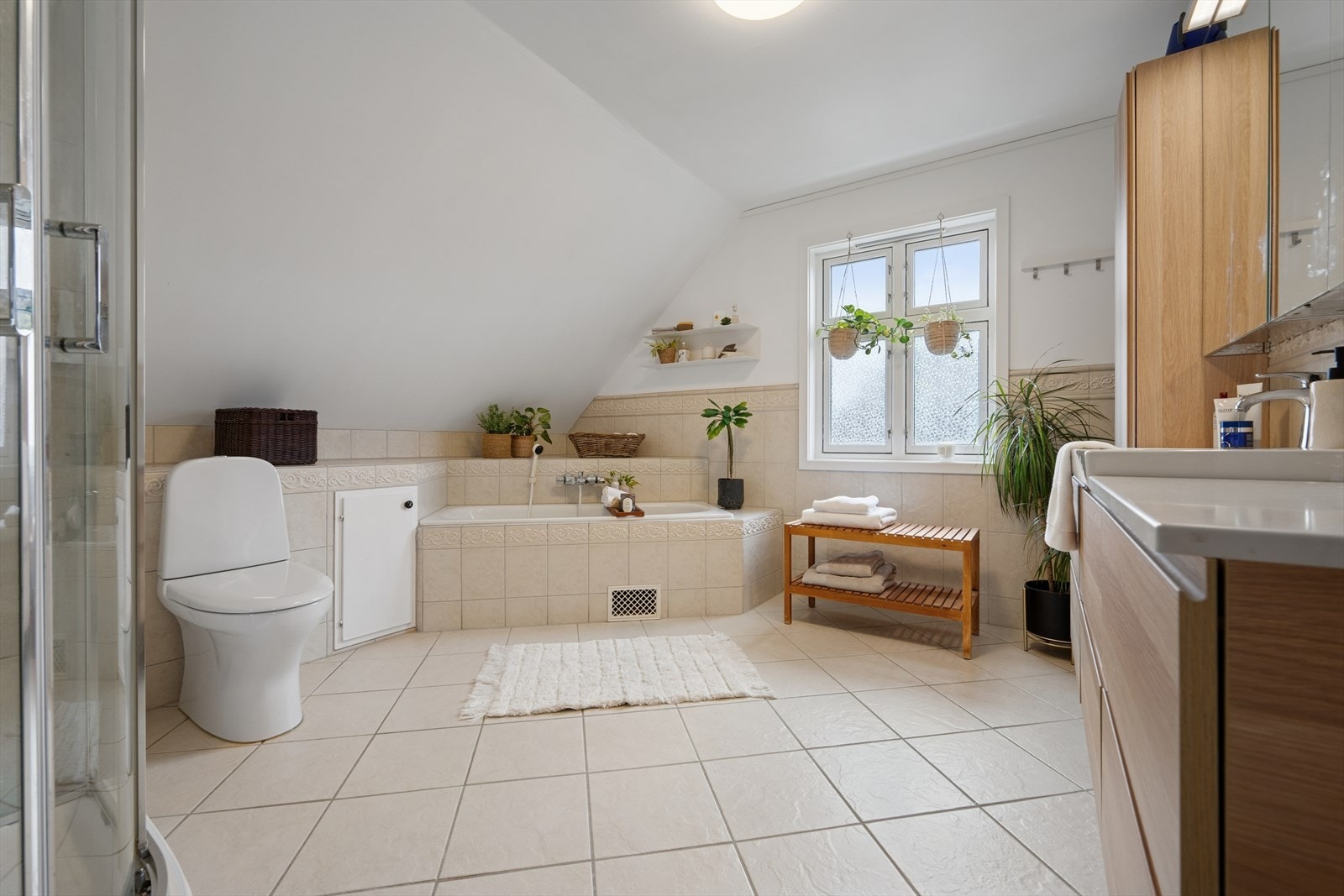 Baderommet er innredet med beige fliser på gulvet og en kombinasjon av beige fliser og malte flater på vegg. I gulvet har man også varmekabler for ekstra komfort. Galleribilde