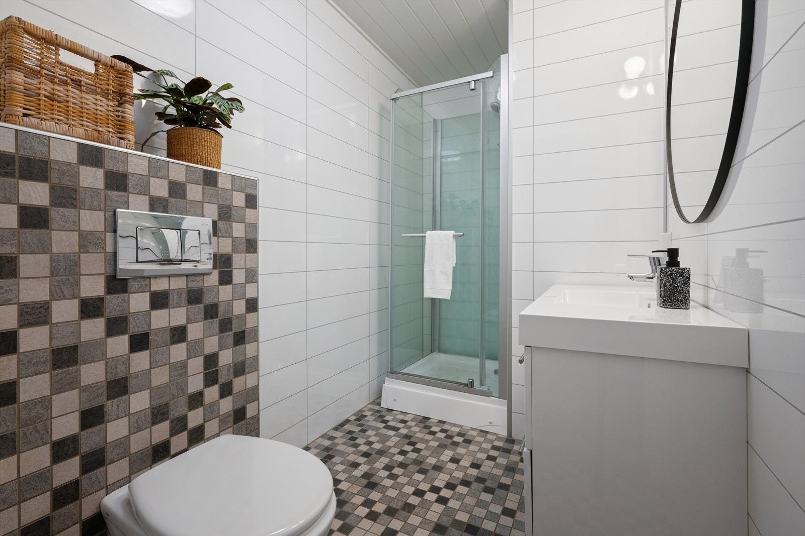 Badet i kjelleren er innredet med hvite baderomsplater på vegg og grå fliser på gulvet. Også her har man varmekabler i gulvet. Badet er ellers utstyrt med dusjkabinett, vegghengt toalett og baderomsinnredning med nedfelt servant. Galleribilde