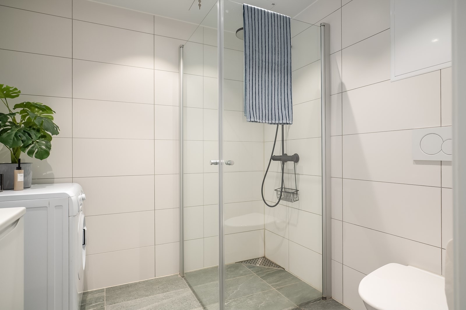 Badet er utstyrt med innfellbare dusjdører, baderomsinnredning, vegghengt klosett og opplegg for vaskemaskin. Galleribilde