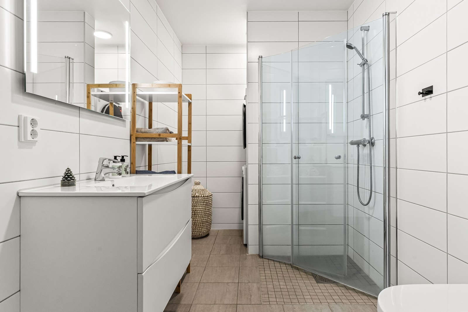 Flislagt bad/wc/vaskerom med varmekabler i gulv. Nedsenket dusjhjørne med glassvegger og veggmontert wc Galleribilde