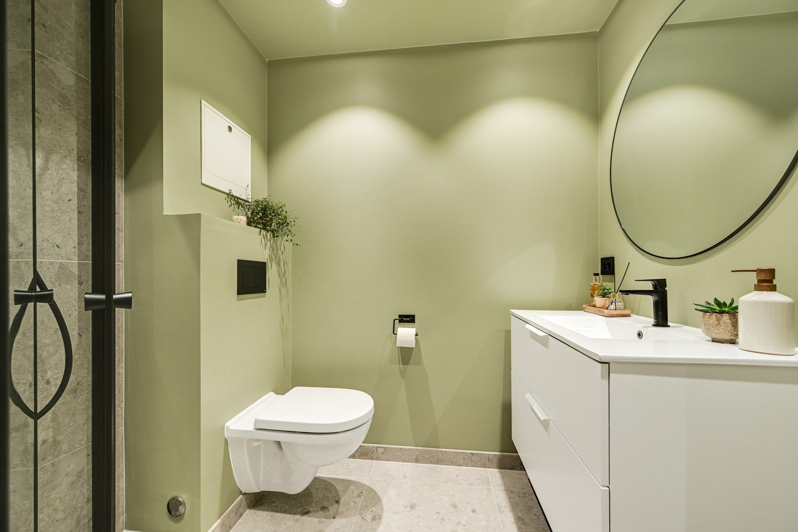 Bad i 2.etg. har malte vegger, malt tak, med spotter, og flis på gulv. Helstøpt servant i skuffinnredning, vegghent toalett og dusj på vegg med glassdører. Galleribilde