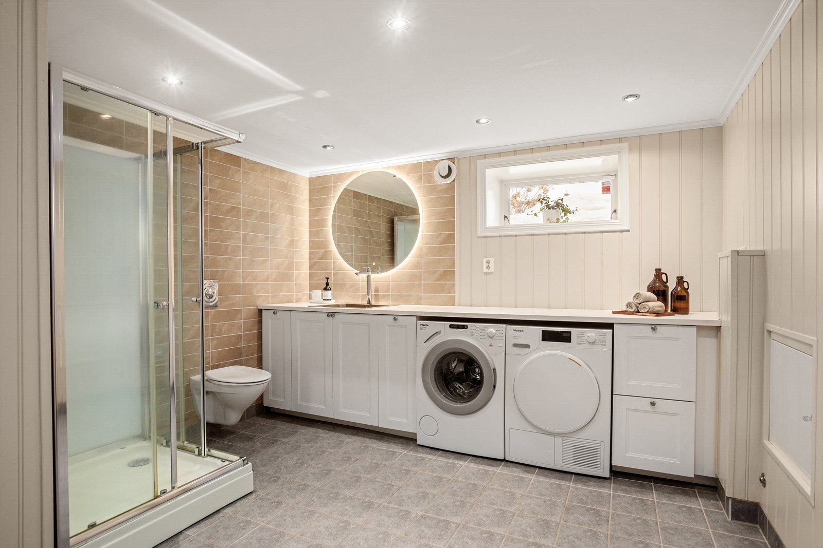 Praktisk og pent bad/vaskerom med flislagte overflater og varmekabler i gulv Galleribilde