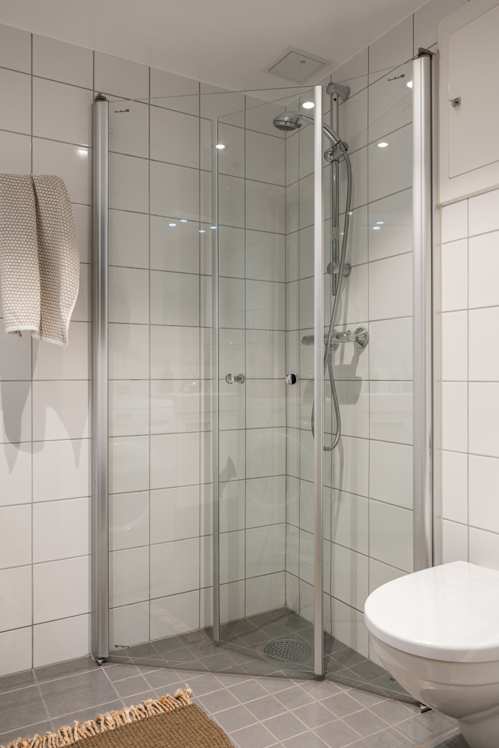 Baderommet er utstyrt med lyst servantskap, speil med belysning over, dusjhjørne med innfellbare glassdører og vegghengt toalett. Galleribilde