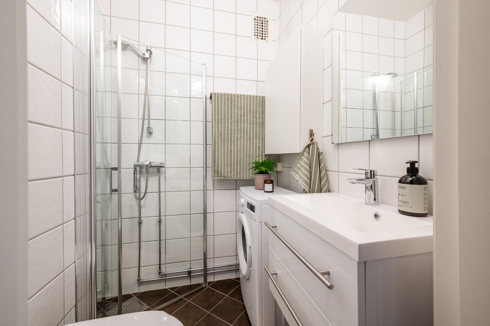 Pent, flislagt baderom med vegghengt innredning med skuffer og tilhørende speil. Galleribilde