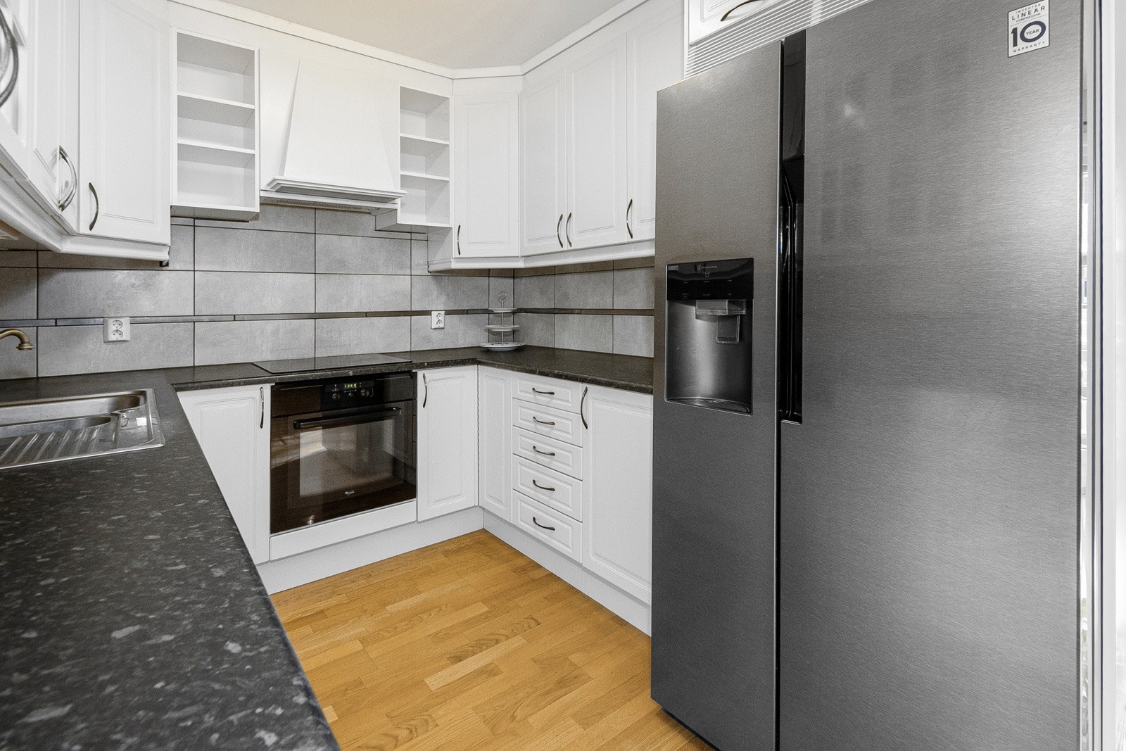 Pen kjøkkeninnredning med profilerte fronter og glass samt laminert benkeplate og flis mellom over- og underskap. Galleribilde