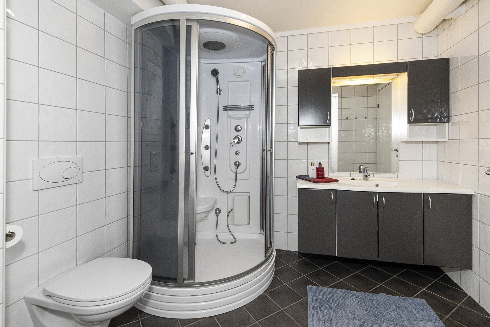 Stort og deilig bad/vaskerom med dusjkabinett, veggmontert toalett og innredning med skap og heldekkende servant. Galleribilde