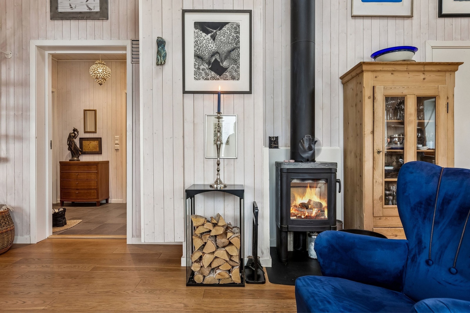 Sett deg gjerne i den blå stolen foran peisovnen eller i den andre stolen for å se inn i flammene. Galleribilde