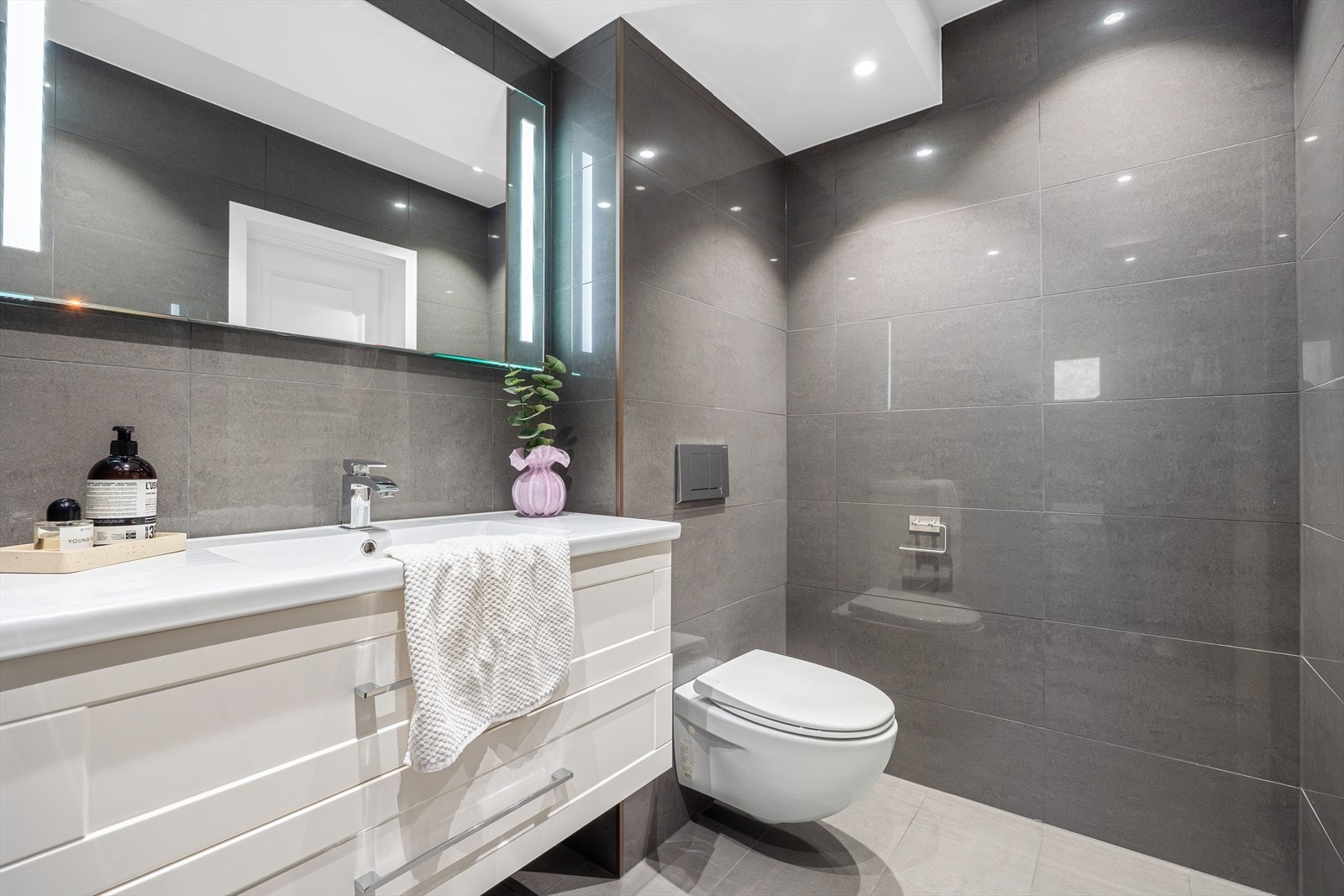 Rommet er innredet med vegghengt toalett, badekar og heldekkende servant og speil med belysning. Galleribilde