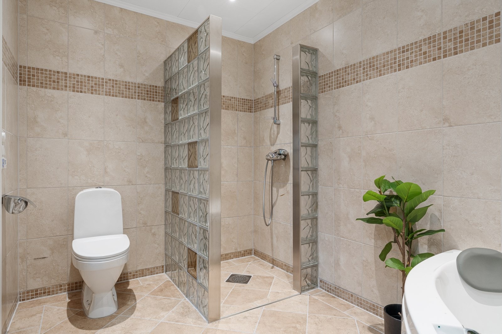 Romslig dusjnisje med glassbyggerstein og flislagt bad med tidløst uttrykk. Galleribilde