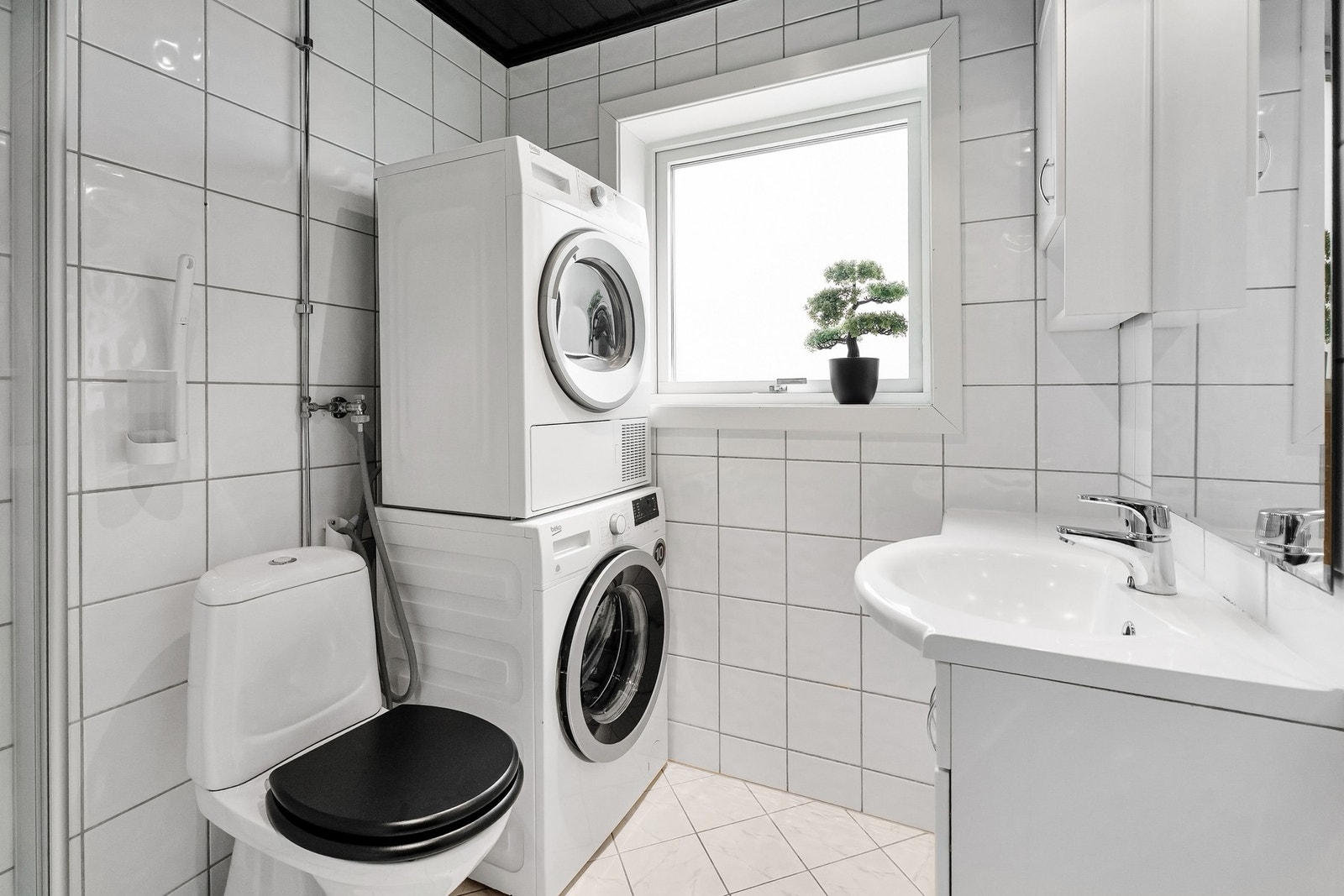 Flislagt bad med opplegg for vaskemaskin, toalett, dusjhjørne, servant og servantskap. Galleribilde