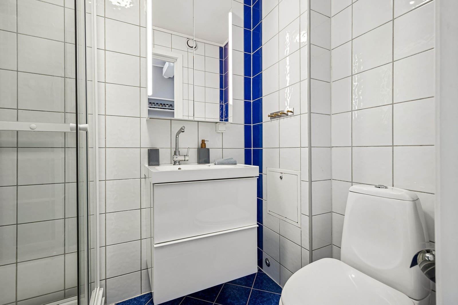 Badet er utstyrt med vegghengt servantinnredning, speilskap med belysning, dusjkabinett og gulvstående toalett. Galleribilde