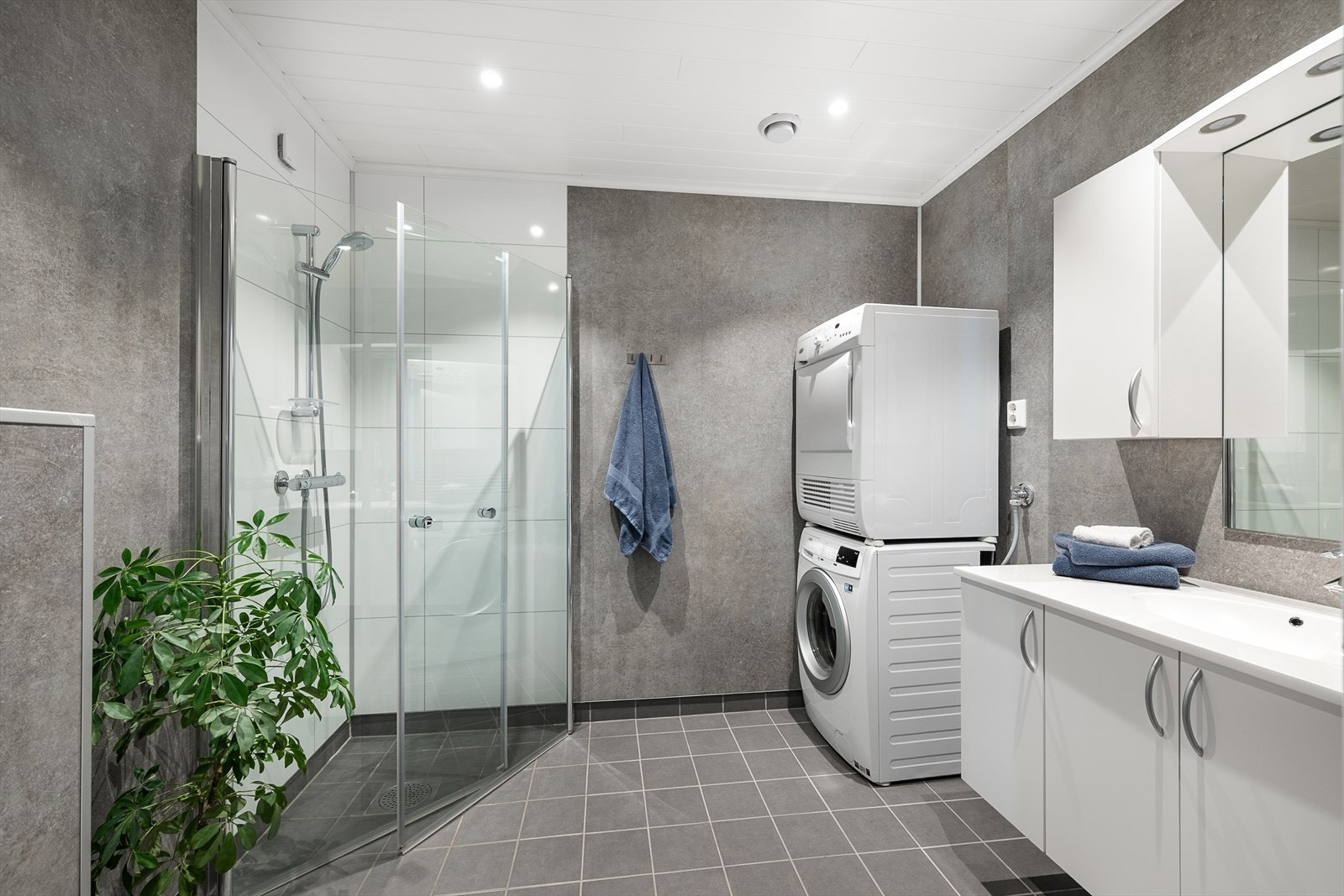 Badet har dusjhjørne med dører i herdet glass og praktisk opplegg for vaskemaskin og tørketrommel. Vegghengt WC. Galleribilde