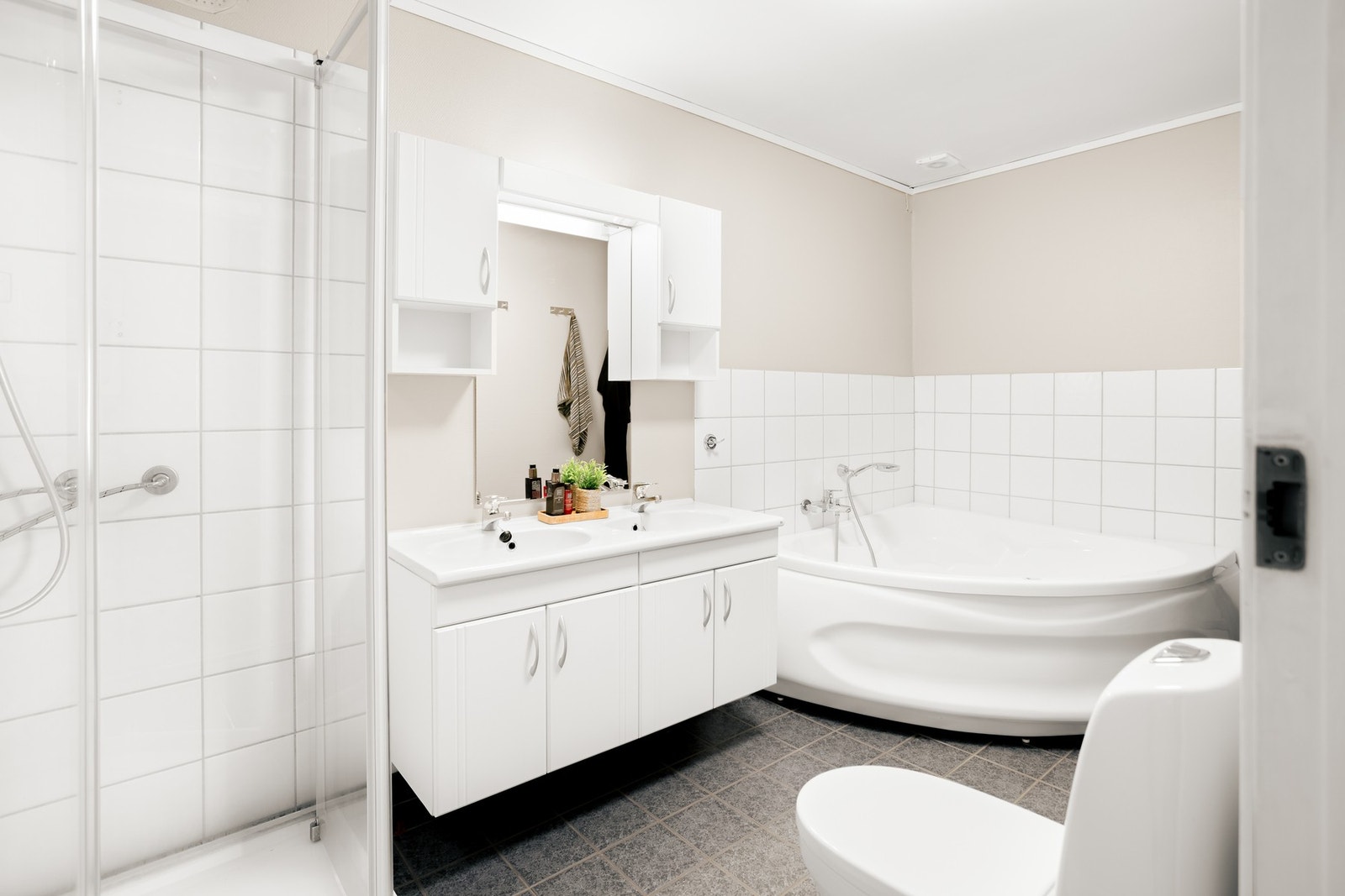 Badet har en romslig utforming og er utstyrt med to nedfelte servanter, toalett, dusjkabinett og badekar. Galleribilde