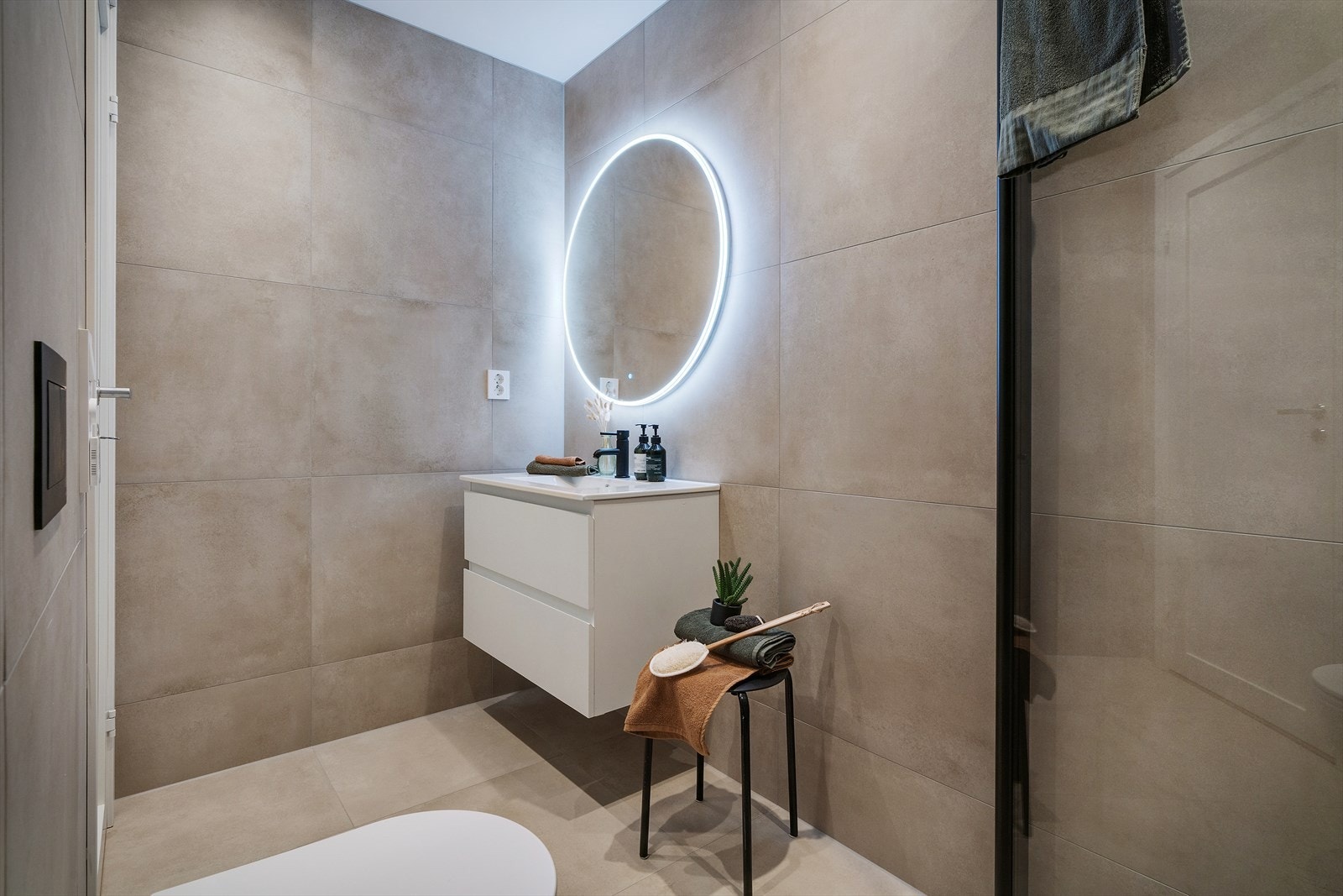 Badet står i stil med resten av boligen, er lekkert helfliset og er innredet med nedfelt servant, veggmontert toalett, dusjvegger og opplegg for vaskemaskin. Galleribilde