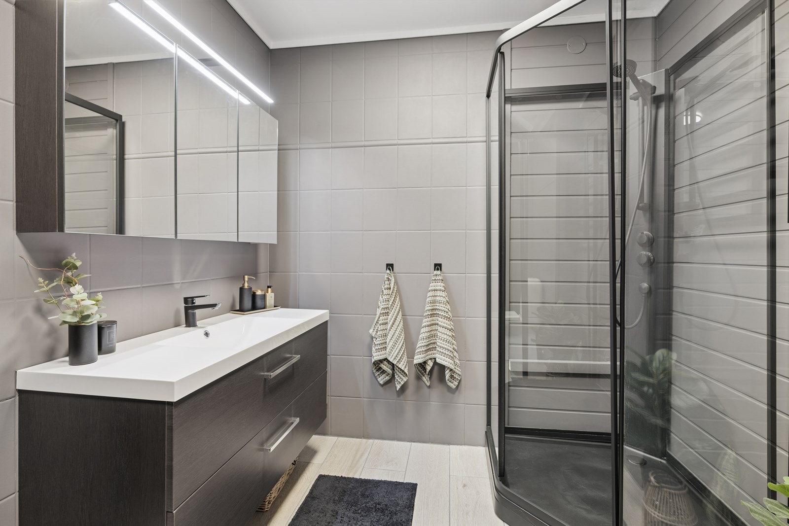 Rommet er innredet med dusjkabinett, toalett, stor baderomsinnredning med hel servant og skuffeseksjon, håndekletørker montert på vegg for den ekte hotellfølelsen i hverdagen og belyst speilskap. Galleribilde