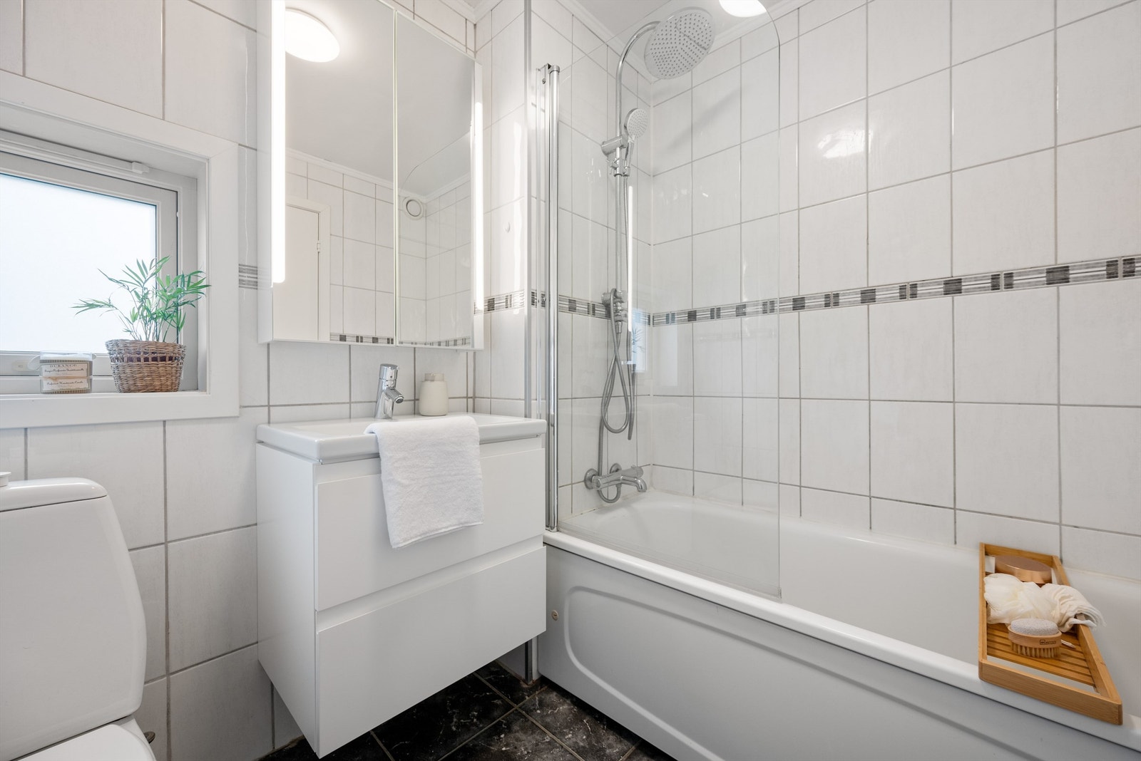 Servant med oppbevaring i skuffer, speil på vegg, toalett og badekar med dusj. Galleribilde