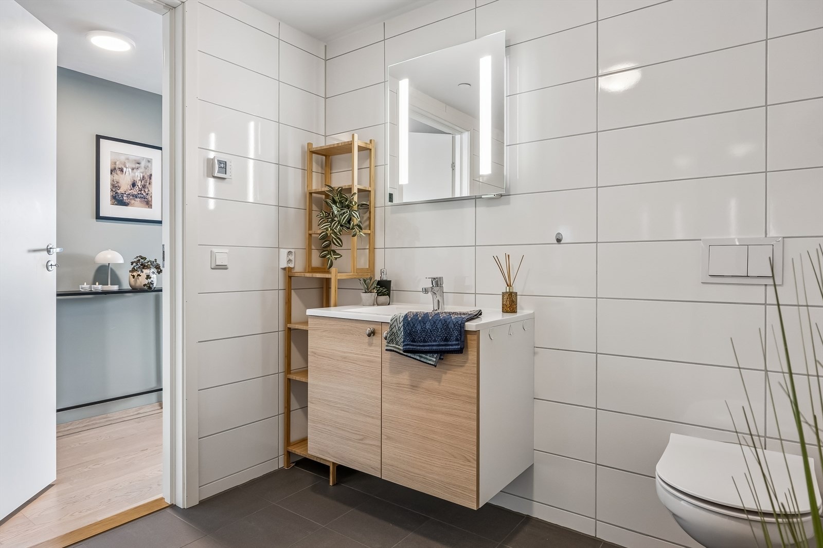 Romslig flislagt bad. Innredning med glatte fronter og heldekkende servant. speil med lys. Galleribilde