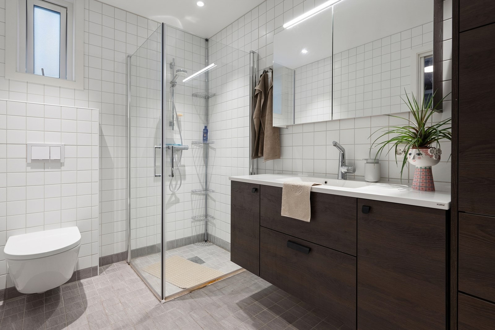 Badet er utstyrt med vegghengt toalett og et dusjhjørne med praktiske, innfellbare glassdører. Galleribilde