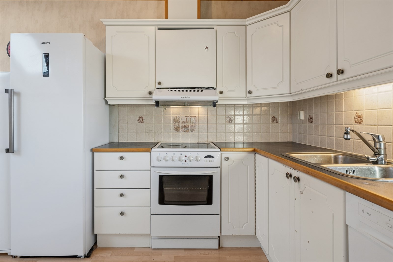 Kjøkkenet ligger delvis tilbaketrukket fra stuen, noe som gir en god avgrensning mellom matlaging og øvrig oppholdssone. Innredningen er fra byggeår og består av profilerte fronter og laminert benkeplate. Galleribilde