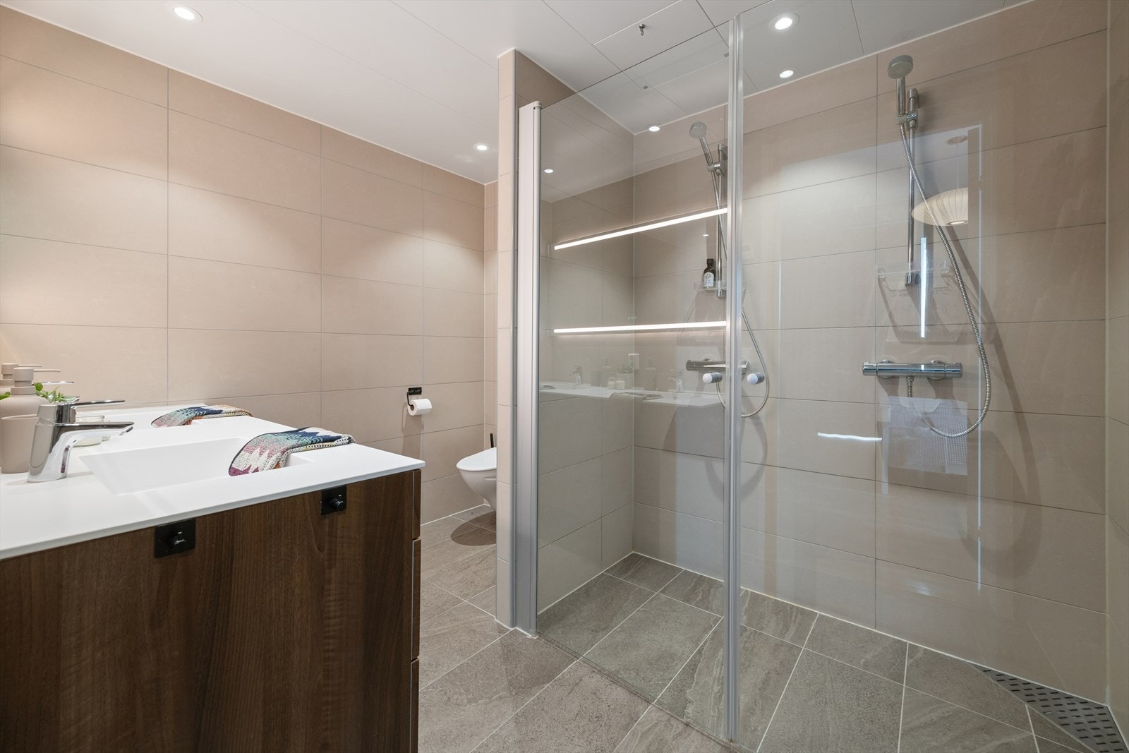 Hovedbadet er flislagt og utstyrt med vegghengt toalett, servantinnredning og en romslig dusjsone. Galleribilde